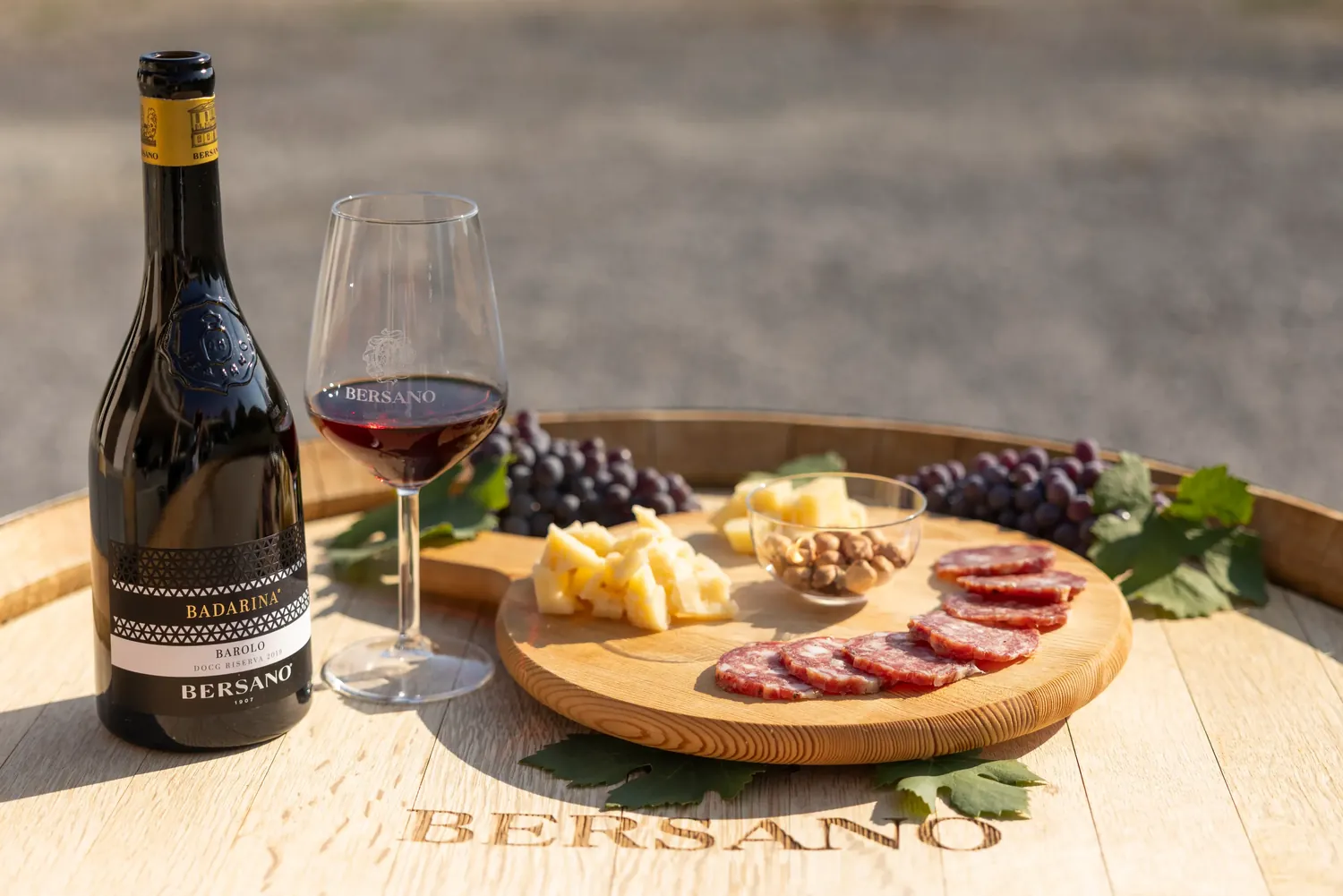 Barolo Badarina con calice, formaggi e salumi su una botte